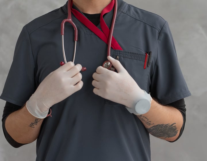 Gloved hands of a provider in scrubs holding a stethoscope